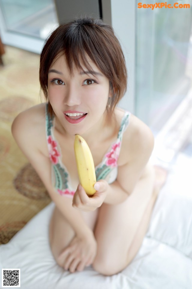 A woman sitting on a bed holding a banana.
