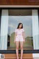 A woman standing in front of a window wearing a pink romper.