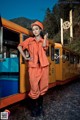 A woman in an orange jumpsuit standing next to a train.