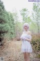 A woman in a white dress standing in the woods.