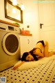 A woman laying on the floor next to a washing machine.