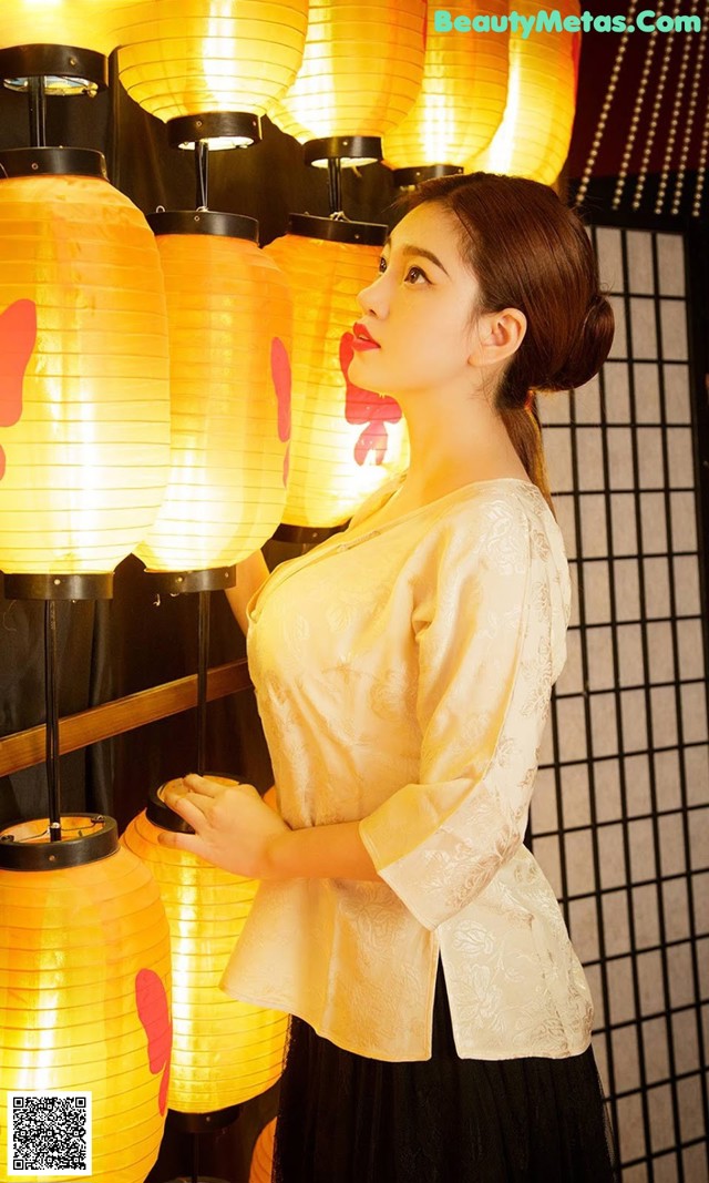 A woman standing in front of a bunch of yellow lanterns.