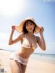 A woman in a bikini and hat on the beach.