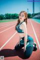 A woman in a sports bra top and leggings crouching on a track.