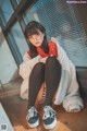 A woman sitting on the floor wearing a white coat and black tights.