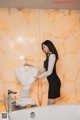 A woman in a black dress standing next to a bathtub.