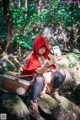 A woman in a red hooded outfit sitting on a rock with a basket.