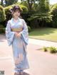 A woman in a blue kimono standing on a sidewalk.